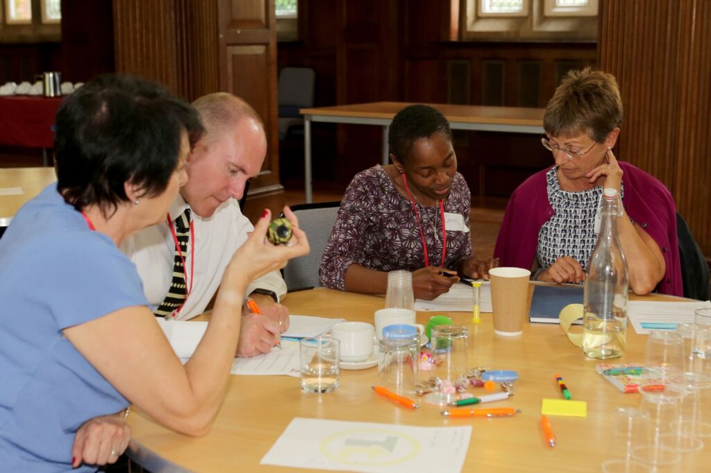 A group of four people is seated around a table, actively engaging in a discussion during a Transform Your Training event. The table is covered with various materials, including papers, pens, and cups.